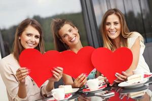 Three girlfriends holding hearts in cafe photo