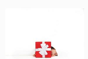 a young man holding a red present box on a white background. child covers his face with a box photo