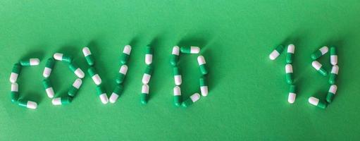 Inscription Covid 19 from letters made of pills on a green background. Corona virus concept. banner photo