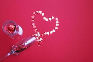 Glass of champagne with red hearts on red background. Valentines background, love, date concept with copy space photo