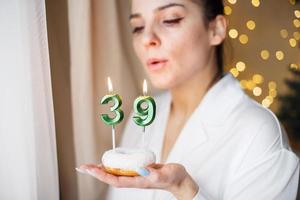 mujer sosteniendo un pastel con las velas número 39 en un fondo bokeh borroso festivo foto