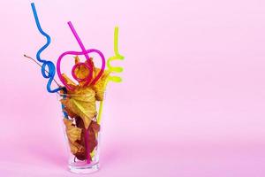 autumn leaf cocktail. autumn leaves in a glass with a straw on a pink background photo