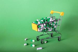 Shopping cart with medical pills on a green background photo