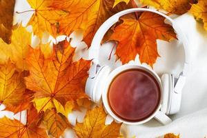 una taza de café o té caliente con hojas de otoño y auriculares sobre un fondo de tela escocesa blanca de punto foto