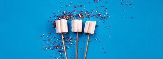 marshmallows composition on wooden skewers on blue background. Flat lay, holiday concept. bouquet of sweets. banner photo