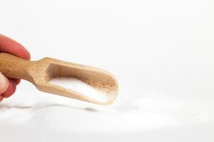 mano con una cuchara de madera de grano de sal sobre fondo blanco foto