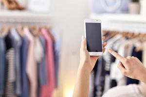 Female hand holding smartphone in clothes shop photo
