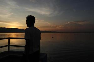 Silhouette of a young man standing by the lake enjoying the sunset. peaceful atmosphere in nature photo