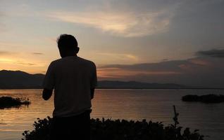 Silhouette of a young man standing by the lake enjoying the sunset. peaceful atmosphere in nature photo