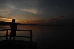 Silhouette of a young man standing by the lake enjoying the sunset. peaceful atmosphere in nature photo