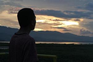 Silhouette of a young man standing by the lake enjoying the sunset. peaceful atmosphere in nature photo