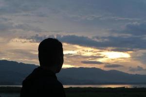 Silhouette of a young man standing by the lake enjoying the sunset. peaceful atmosphere in nature photo