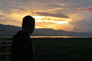 Silhouette of a young man standing by the lake enjoying the sunset. peaceful atmosphere in nature photo