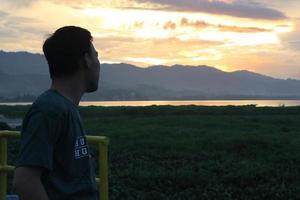 Silhouette of a young man standing by the lake enjoying the sunset. peaceful atmosphere in nature photo