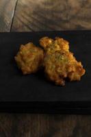 Bakwan Jagung or corn fritters is on a black cutting board against a wooden background photo