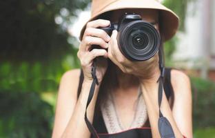 mujer asiática con sombrero y top sin mangas tomando fotos en el parque con cámara dslr. enfoque selectivo en la lente