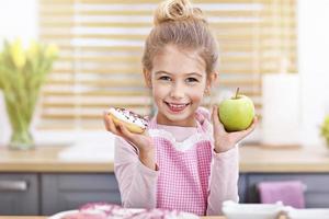 linda niña eligiendo entre manzana y donut en la cocina foto