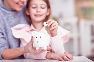 Young girl and her mother with piggybank sitting at table photo