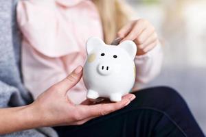 Young girl and her mother with piggybank sitting at table photo