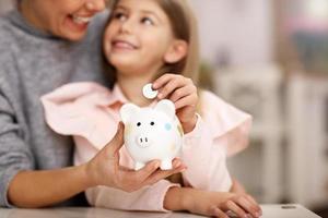 Young girl and her mother with piggybank sitting at table photo