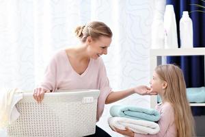 Beautiful young woman and child girl having fun while doing laundry at home photo