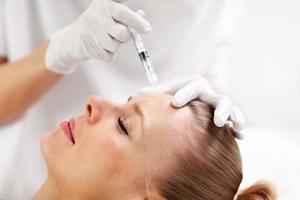 Close up of hands of cosmetologist making botox injection in female forehead photo