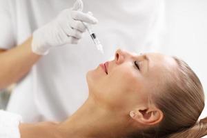 Close up of hands of cosmetologist making botox injection in female lips photo