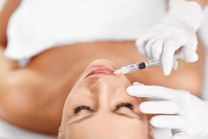 Close up of hands of cosmetologist making botox injection in female lips photo