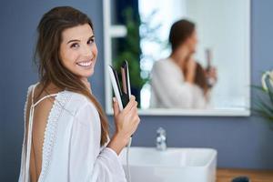 Beautiful brunette woman straightening hair in the bathroom photo