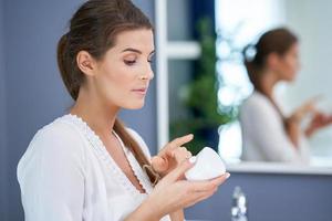 Beautiful brunette woman applying face cream in the bathroom photo