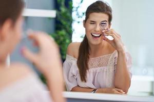 hermosa mujer morena con rizador de pestañas en el baño foto