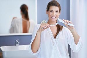 Beautiful brunette woman brushing teeth in the bathroom photo