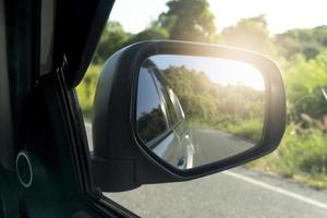 Mirror view of car travel on the asphalt road. with blurred of green grass at day. photo