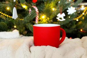 taza roja en blanco con árbol de navidad en el fondo, taza de té o café con decoración de navidad y año nuevo, maqueta horizontal con taza de cerámica para bebidas calientes, plantilla de impresión de regalo vacía. foto