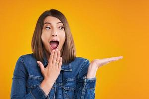 Close up of woman in denim jacket thinking and pointing over yellow background photo