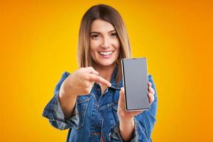 Close up of woman in denim jacket with smartphone over yellow background photo