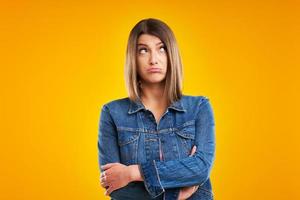 Close up of woman in denim jacket thinking and pointing over yellow background photo