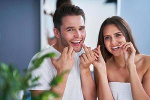 Portrait of happy young couple flossing teeth in the bathroom photo