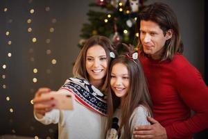 hermosa familia celebrando la navidad en casa y tomando selfie foto