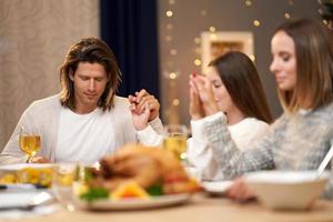 hermosa familia rezando durante la cena festiva en casa foto