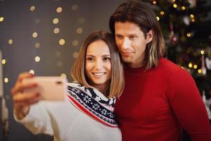 hermosa pareja celebrando la navidad en casa y tomando selfie foto