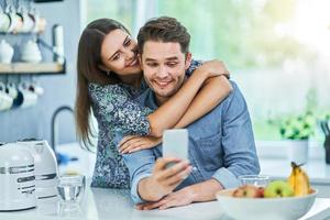 Couple in home kitchen using smartphone photo