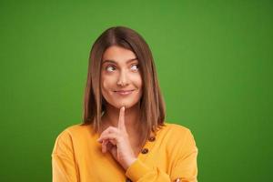 Close up of woman in yellow sweater thinking and pointing over green background photo