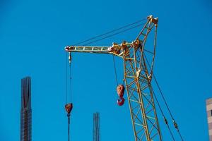 High-rise construction crane with a long yellow boom against the blue sky. photo