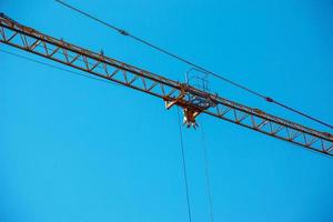 High-rise construction crane with a long yellow boom against the blue sky. photo