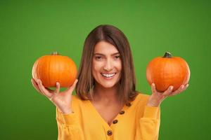 Close up of woman in yellow sweater holding pumpkin over green background photo