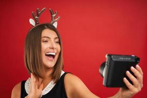mujer adulta feliz en estado de ánimo navideño tomando fotos instantáneas sobre fondo rojo