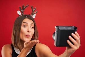 Adult happy woman in Christmas mood taking instant pictures over red background photo