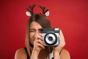 mujer adulta feliz en estado de ánimo navideño tomando fotos instantáneas sobre fondo rojo