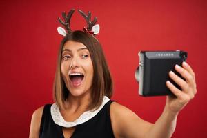Adult happy woman in Christmas mood taking instant pictures over red background photo